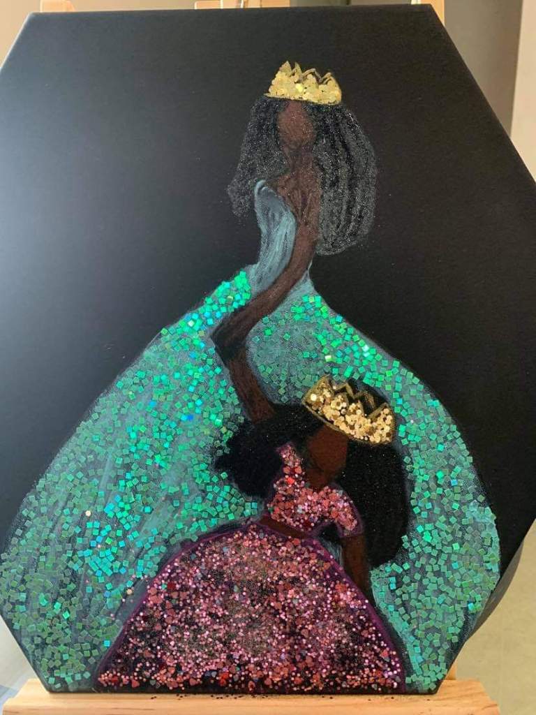 Svart mor och dotter som håller varandra i handen och bär glittriga kronor och balklänningar.