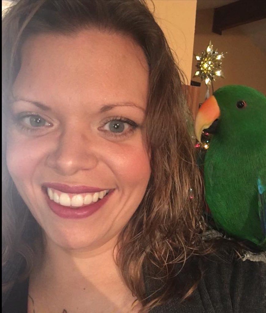 אישה לטינית מחייכת למצלמה עם תוכי על כתפה