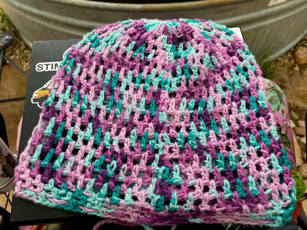 Slouchy beanie with a loose weave and variable pink and green coloring sitting on a table