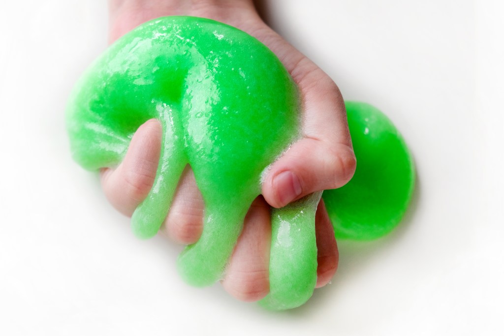 Hand squeezing textured slime with bubbles, stretching the gooey substance. Female teen hand holding blue shining slime, squeezing it. Adorable Girl stretching slime toy to the sides. Liquid toy.