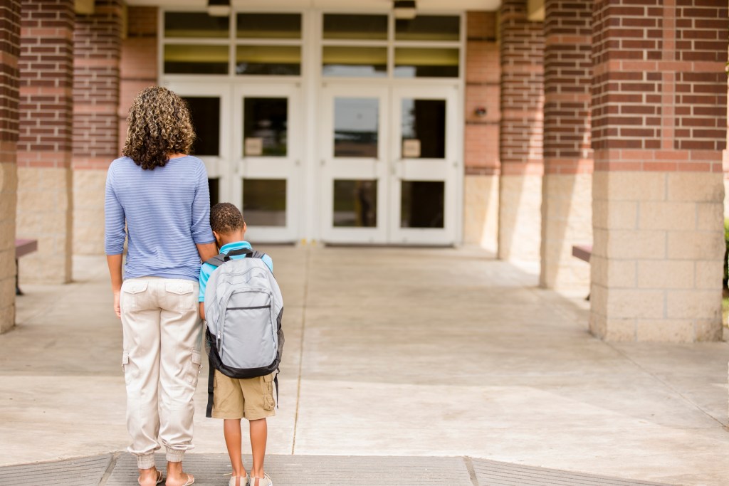 Nervous boy. First day of school. Holds on to mom while standing in front of the doors into the school