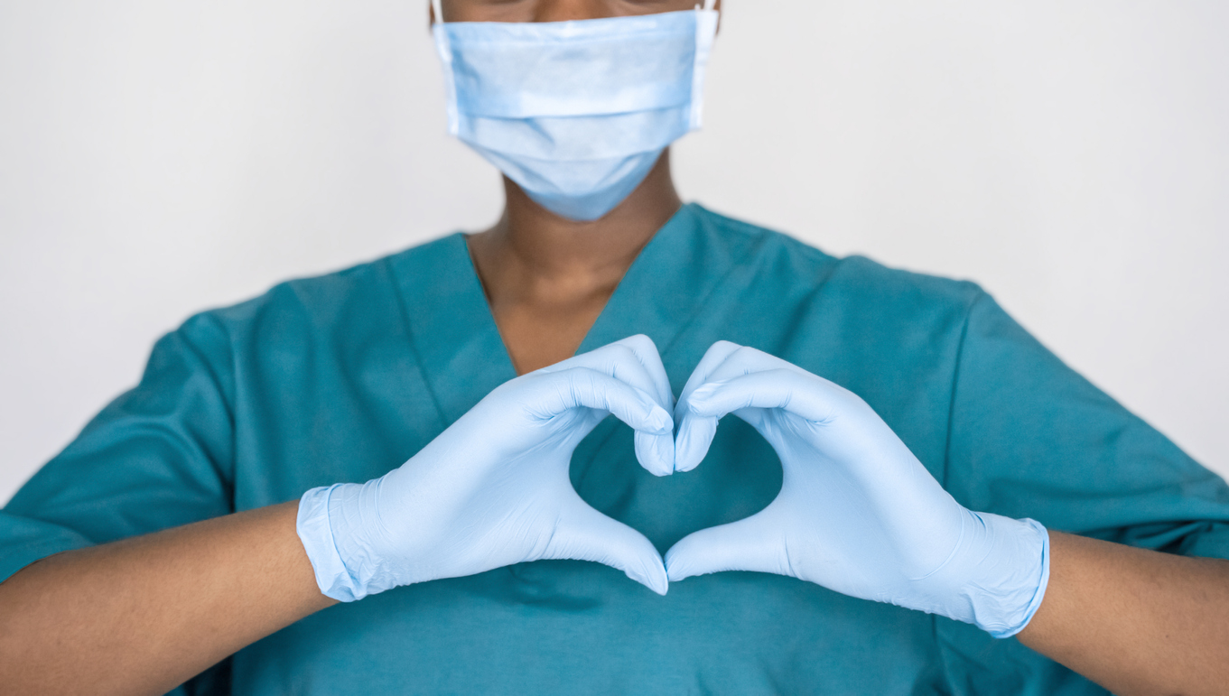 Female african professional medic nurse wear face mask, gloves, blue green uniform showing heart hands shape. Medical love, care and safety symbol, corona virus health protection sign concept.
