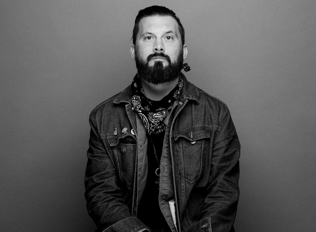 גבר לבן עם שיער קצר וזקן לבוש ז'קט ג'ינס מביט ישירות במצלמה