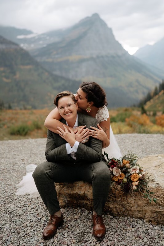 Two women hugging and kissing for a wedding photo in front of a mountain