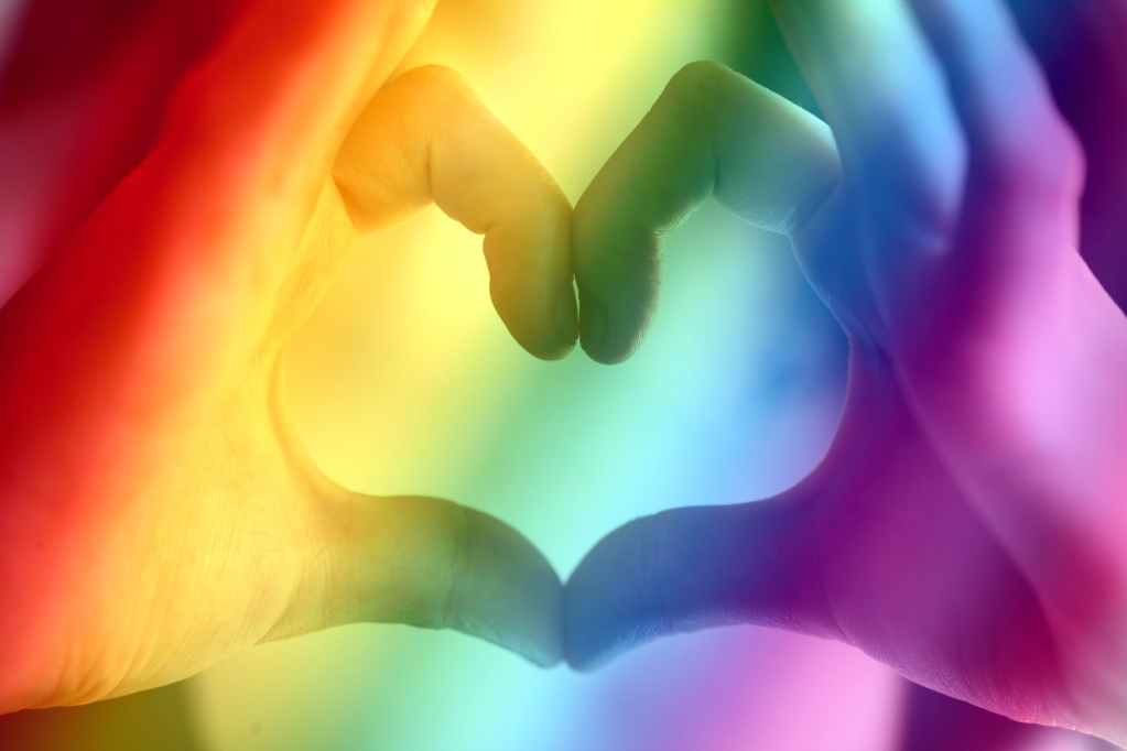 Fingers bathed in rainbow light form a heart shape