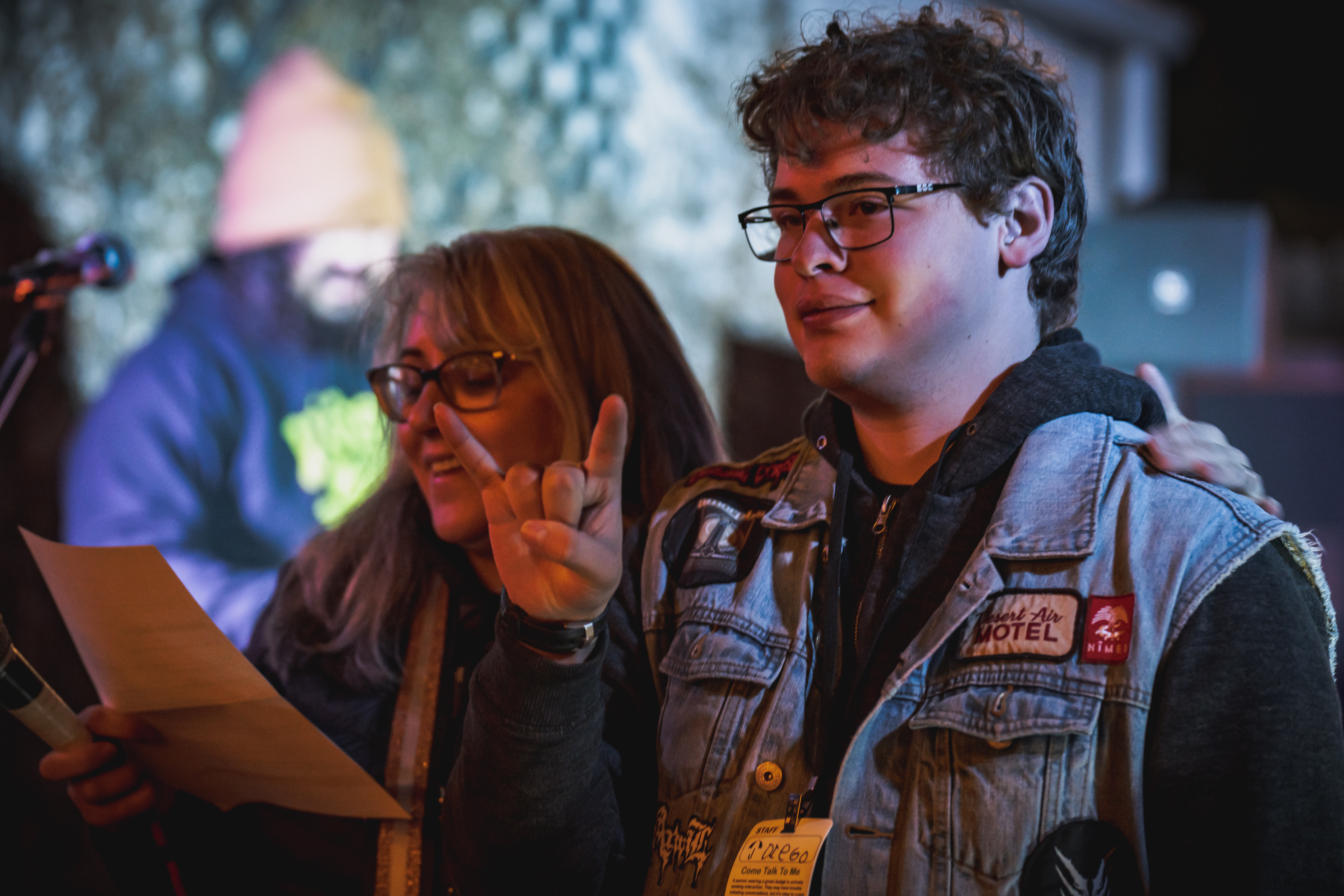 A middle-aged white woman and a white teenage man address a crowd at a microphone