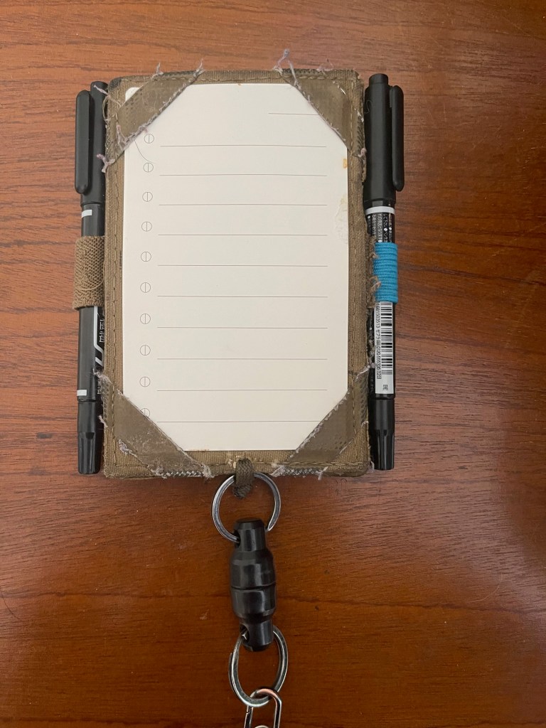 Analog index card in an index card holder with two black markers on each side in pen loops. A magnetic quick connect is attached to the bottom of the card holder.