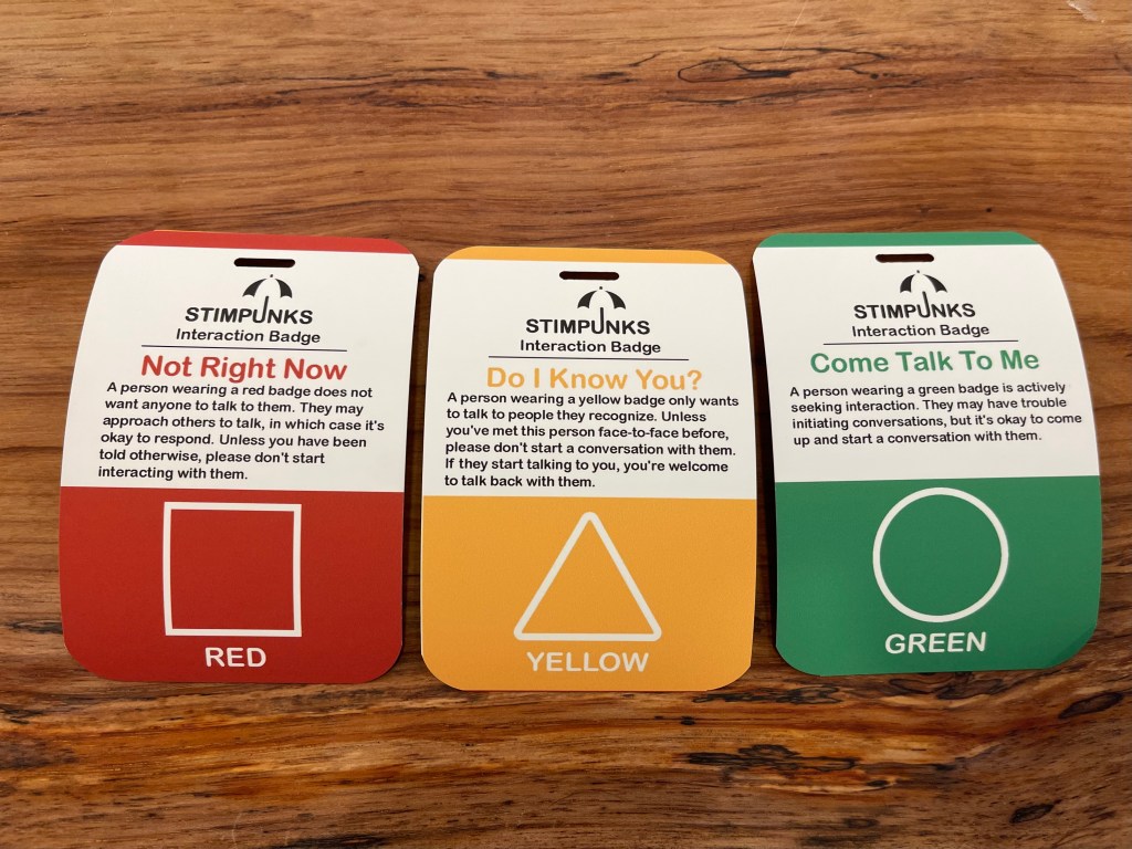 Red, yellow, and green interaction badges printed on poly paper arranged side-by-side on a wooden table