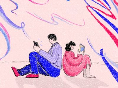 Two people sit back to back on a floor, one reading a book, the other reading a tablet