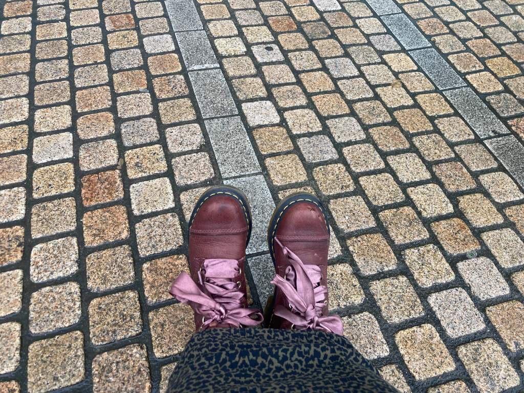 Top down shot of burgundy red Doc Marten boots with light red ribbon shoe laces on a cobbled pathway