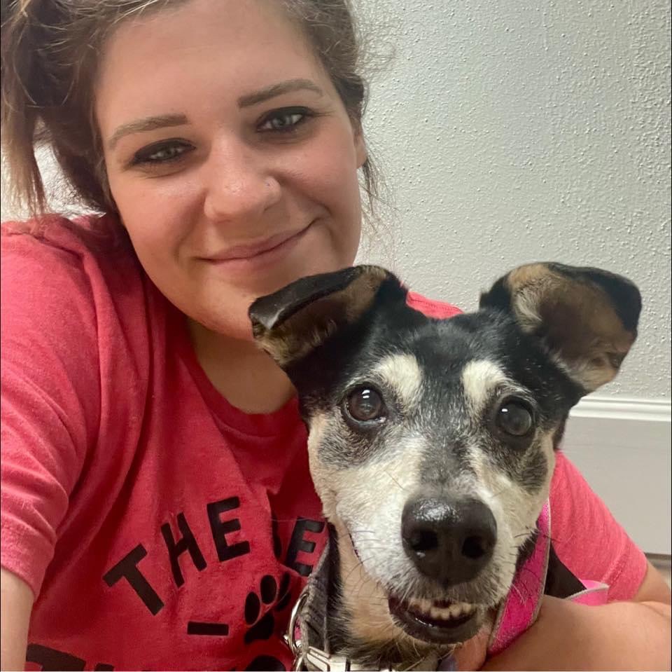 אישה לבנה עם שיער חום מחייכת למצלמה כשהיא מחזיקה כלב