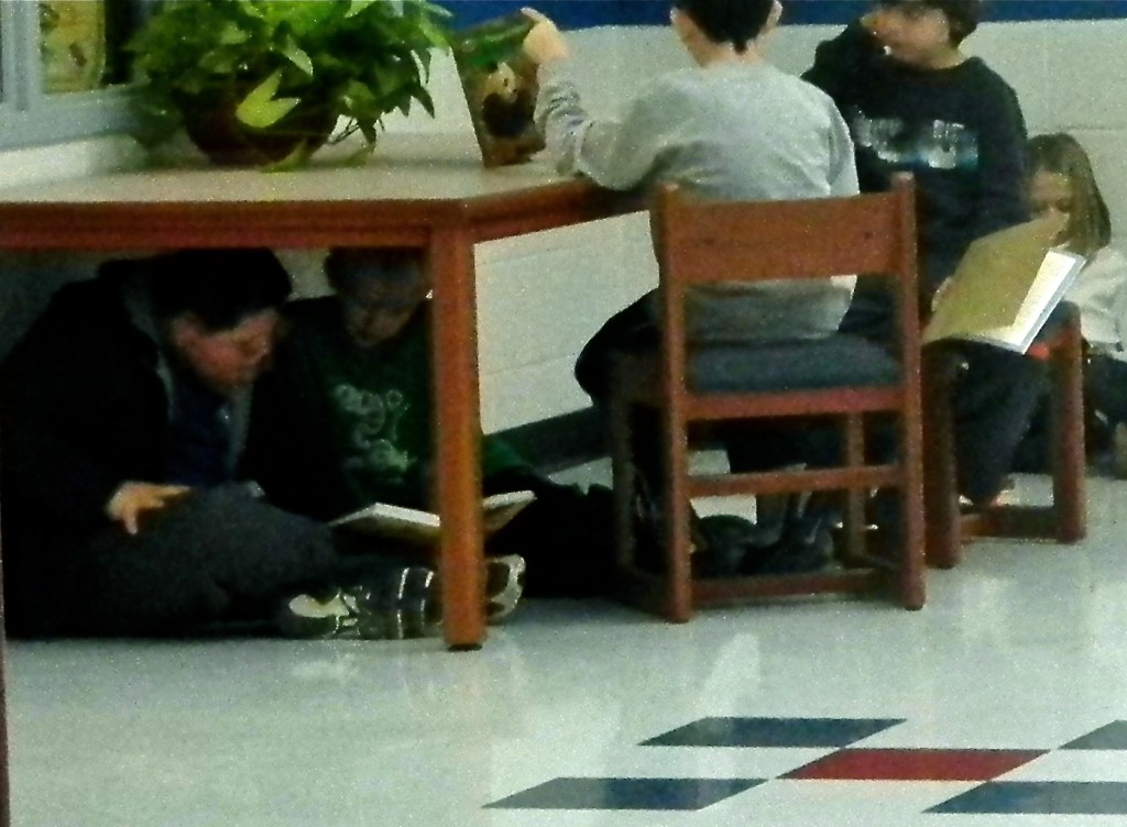 Kids sitting at and under a table in a classroom, learning.