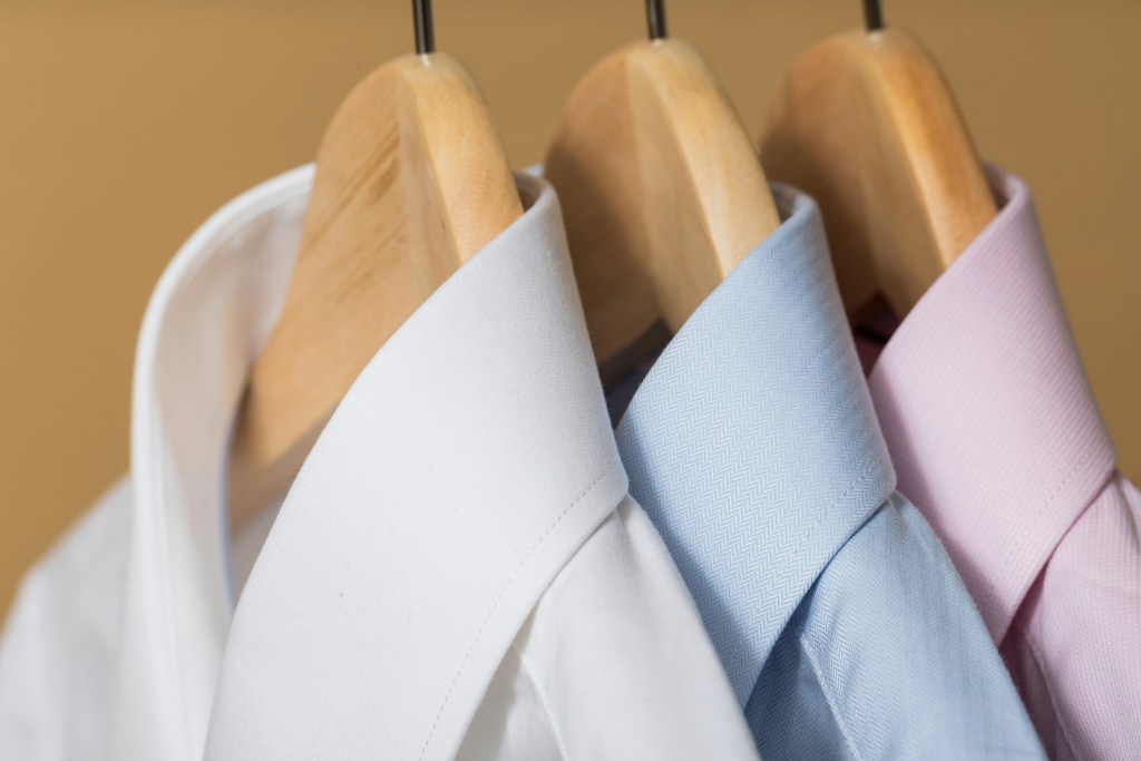Three dress shirts on wooden hangers - one white, one blue, one pink