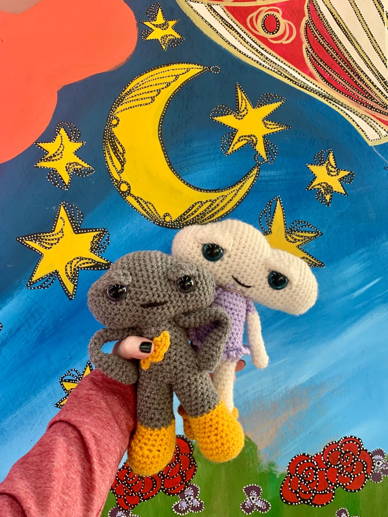 Crochets aliens held up in front of a star and moons illustration